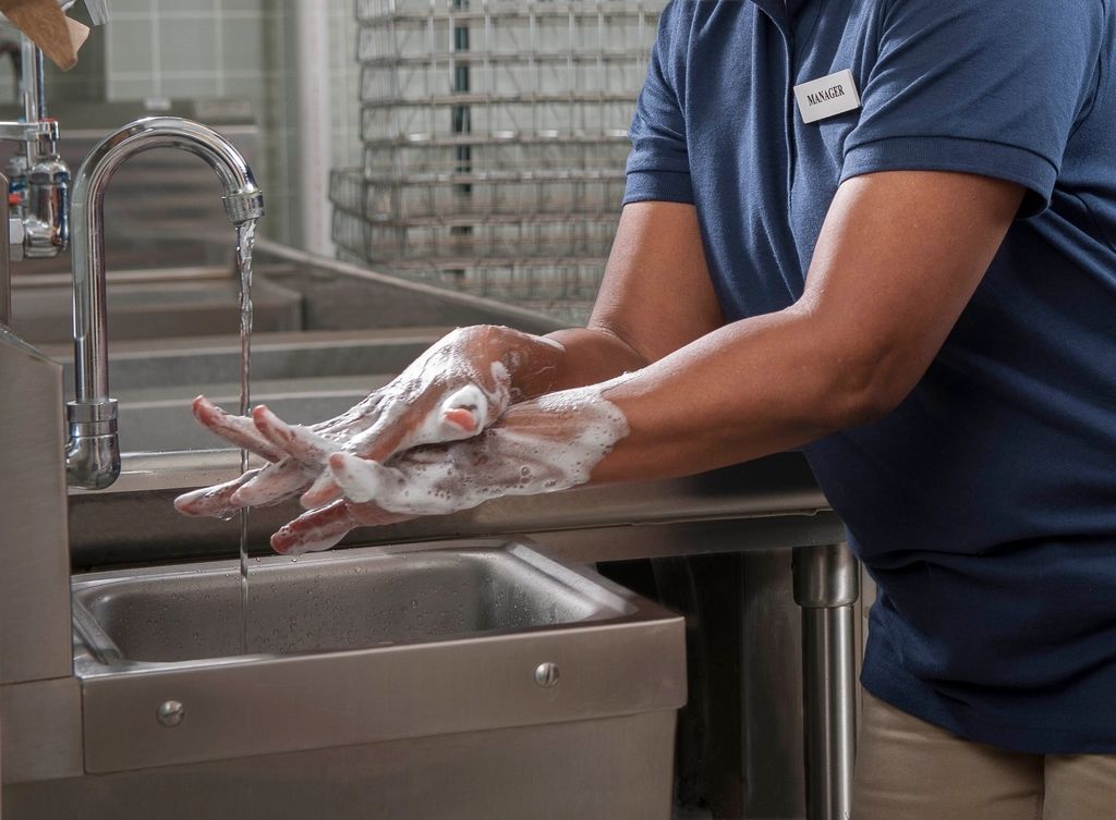 Pekerja dapur mencuci tangan dengan sabun di sinki
