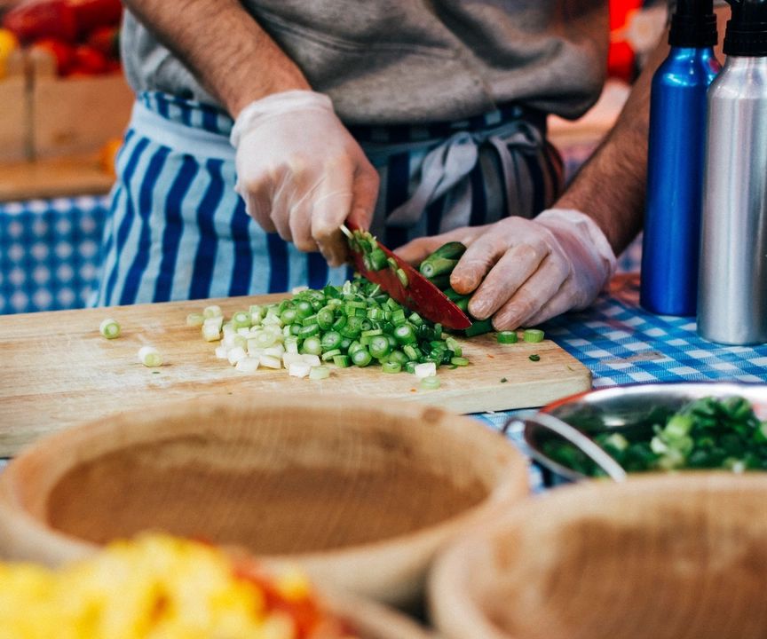 Pengendali makanan memakai sarung tangan sambil memotong daun bawang